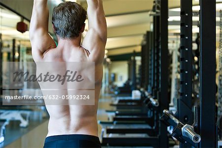 Barechested man stretching in weight room, rear view