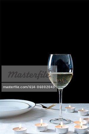 Glass of white wine and tea lights on table