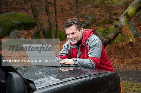 Mature man using laptop on car bonnet