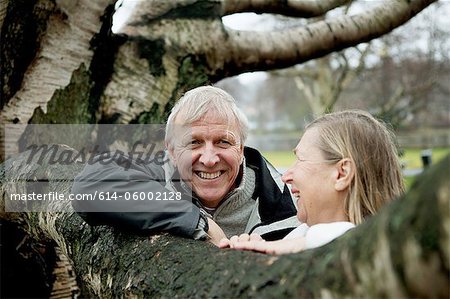 Senior couple leaning against tree, smiling