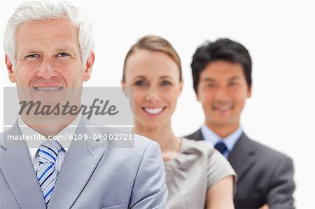 Close-up of a smiling business man with subordinates behind him against white background