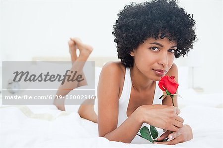 Portrait d'une femme aux cheveux noire, sentant une rose en position couchée sur son lit
