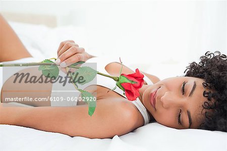 Frizzy haired woman lying on her bed with a rose in a bright room