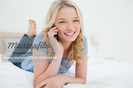 Eine Frau auf dem Bett als She lächelt, wir freuen uns, gleichzeitig ein Phonecall entspannenden.