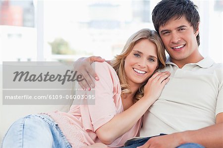 Un homme avec son bras autour d'elle comme elle se repose contre lui sur le canapé, les deux souriant