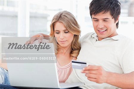 Embracing man and woman use the credit card and laptop together while sitting on the couch.