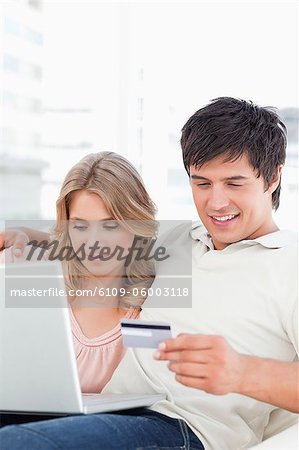 A close up shot of a man and woman using the credit card and laptop while sitting on the couch together.