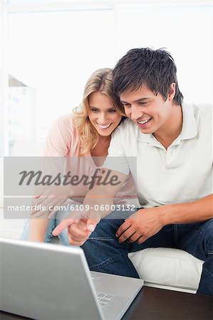A man and woman smiling together on the couch as they look at the laptop screen.