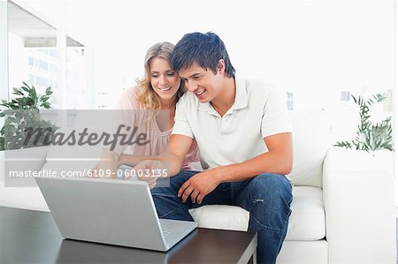 A man and woman using a laptop as they sit on the couch smiling.