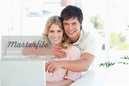 A man holds a woman as they use the laptop together and look in front of them.