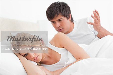 Un homme se disputer avec une femme qu'ils se trouvaient dans le lit. la femme avec sa tête détourné de l'homme.