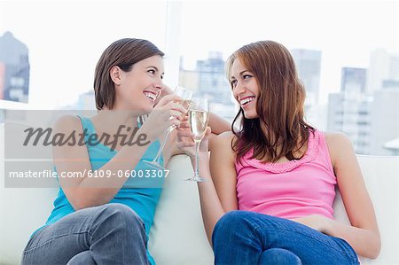 Young smiling women clinking glasses of champagne while looking at each other