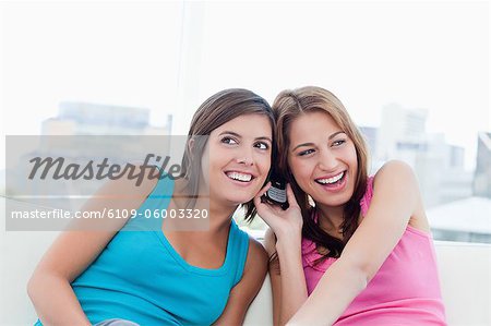 Teenagers smiling while listening to a phone and sitting on a white sofa