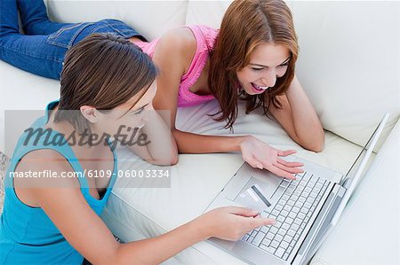 Jeune femme tenant une carte de crédit tout en regardant un ordinateur portable avec un ami sur un canapé