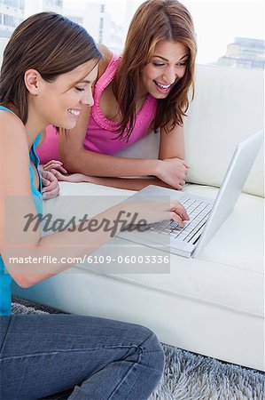 Laptop on a comfortable sofa and used by two smiling young women