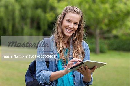 Young happy girl looking at the camera while using her tablet pc in the countryside