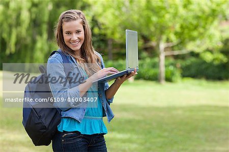 Young happy girl holding her laptop while standing upright in the countryside