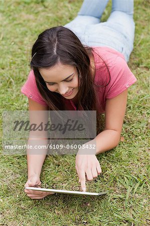Young happy woman lying down in a parkland while using her tablet computer