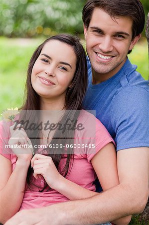 Jeune couple heureux montrant leur bonheur en se tenant debout dans un parc avec une fleur