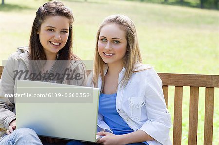 Jeunes filles en regardant la caméra tout en maintenant un ordinateur portable et assis sur un banc