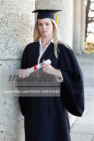 Young serious graduating student looking at the camera while holding her diploma