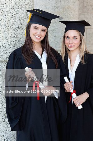 Young smiling graduating students looking at the camera while holding their diplomas