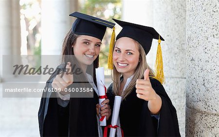 Lächelnd Absolventen ihre Daumen aufstellen beim Betrachten der Kamera