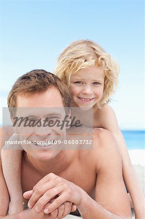 Kleiner Junge auf seinen Vätern wieder am Strand liegend
