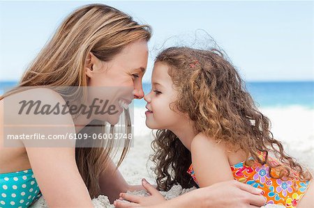 Happy young mother and daughter lying on the beach