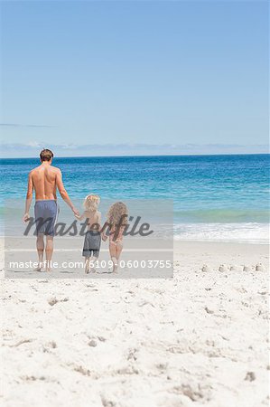 Jeune père et ses enfants marchant vers la mer