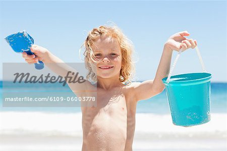 Garçonnet souriant avec un seau et la pelle sur la plage