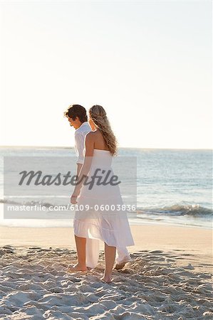 Jeune couple marchant le long du bord de mer vers le coucher du soleil