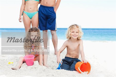 Little children building sandcastles with their parents behind them