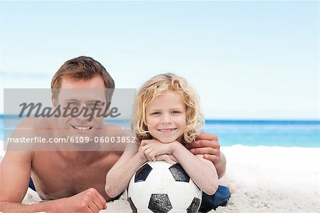 Kleiner Junge mit dem Fußball mit seinem Vater am Strand liegend