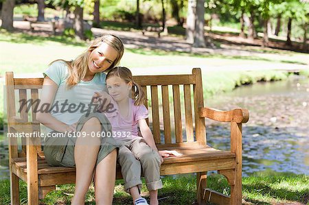 Une mère et une fille souriant assis sur un banc ensemble comme les points de la jeune fille à quelque chose