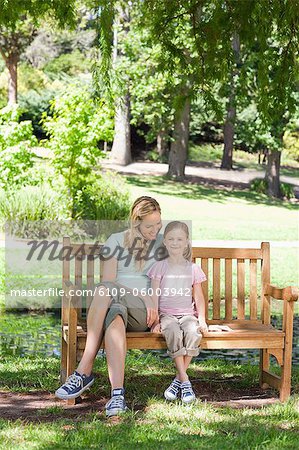 A smiling mother looks at her smiling daughter as they both sit on the park bench