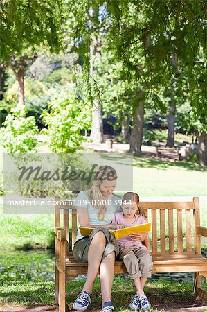 Une mère et une fille souriante tout en étant assis sur le banc de parc lire ensemble