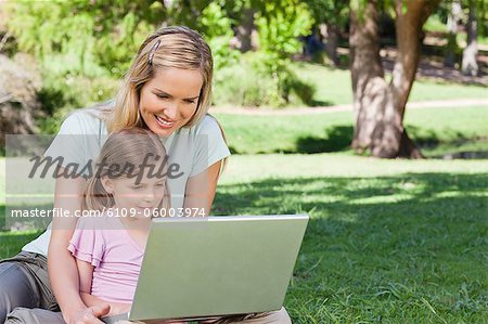 A smiling mom and her child use the laptop together in the park