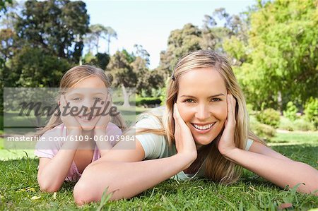 While lying down a smiling mom and her kid rest their heads in their hands