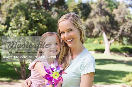 A smiling mother hugging her child who is holding a pin-wheel in front of them