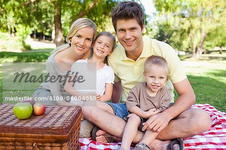 A joyful family sitting on the blanket of their picnic while looking straight ahead