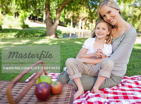 Eine lächelnde Mutter und ihre Tochter sitzt auf der Decke mit ihren Picknickkorb und einige Äpfel