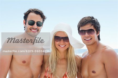 Two men and a woman smiling while wearing sunglasses on a beach