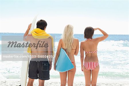 Three people standing at the beach with surfboards looking out to the ocean for a good wave.
