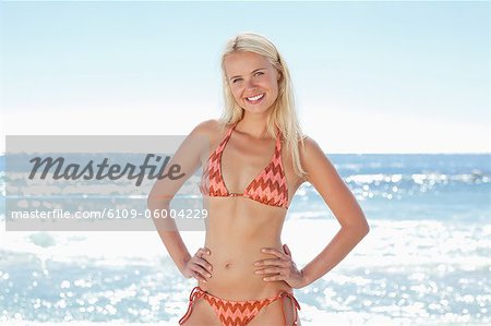 Femme dans un bikini en souriant qu'elle place ses mains sur ses hanches et s'incline sa tête sur le côté