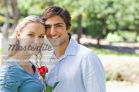 Smiling young couple together in the park with a rose