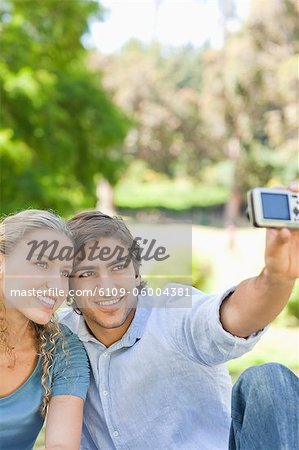 Jeune couple dans le parc en prenant une photo d'eux-mêmes le sourire