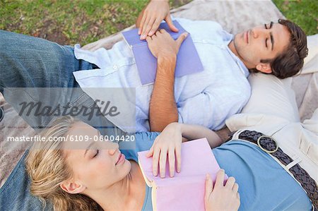 Young couple sleeping while reading in the park