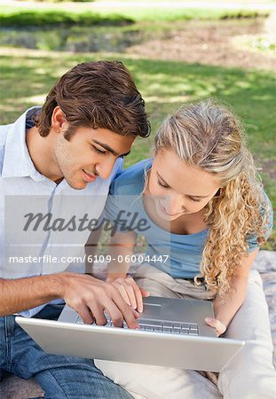 Jeune couple à l'aide de leur ordinateur portable dans le parc