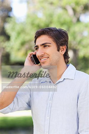 Sourire de jeune homme sur son téléphone mobile dans le parc